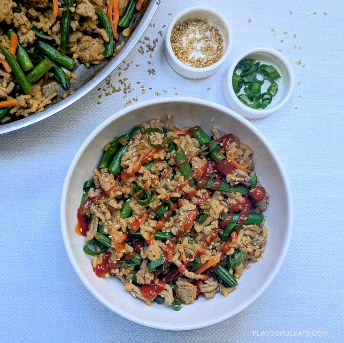 Gochujang Ground Turkey, Rice & Green Bean Skillet in a bowl with sriracha on top.