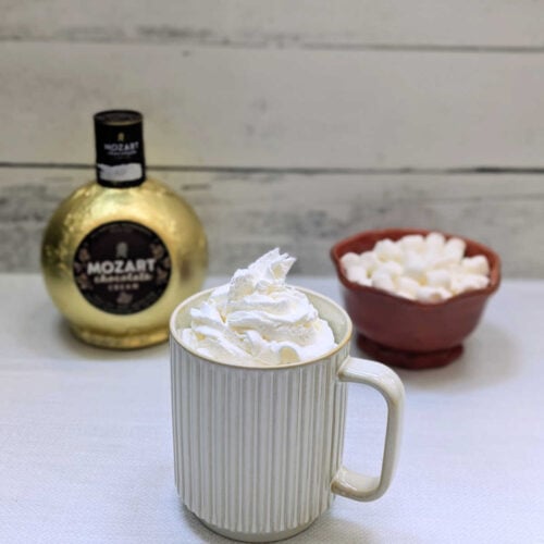 Slow Cooker Boozy Chocolate Coffee in a mug with a bowl of marshmallows and a bottle of chocolate liqueur beside it.