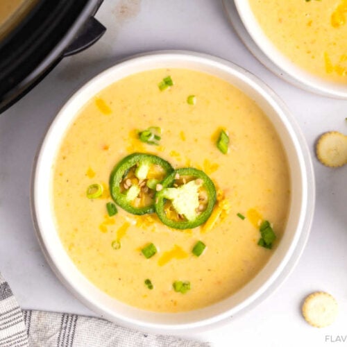 Slow Cooker Jalapeno Cheddar Potato Soup in a bowl garnished with cheddar cheese, sliced jalapeno, and scallions.