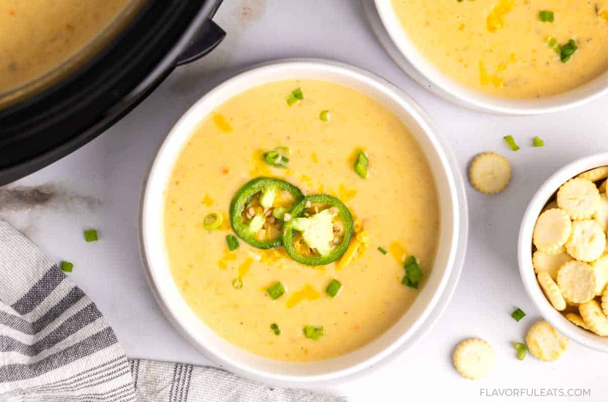 Slow Cooker Jalapeno Cheddar Potato Soup in a bowl garnished with cheddar cheese, sliced jalapeno, and scallions.