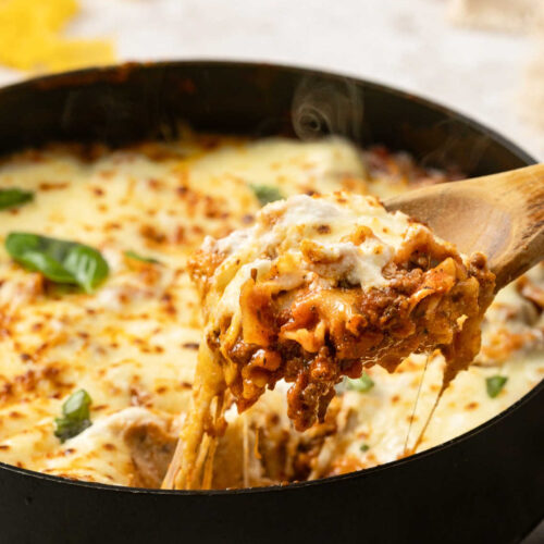 A serving spoon with a cheesy pull of One-Pan Cheesy Lasagna Skillet coming out of the pan.