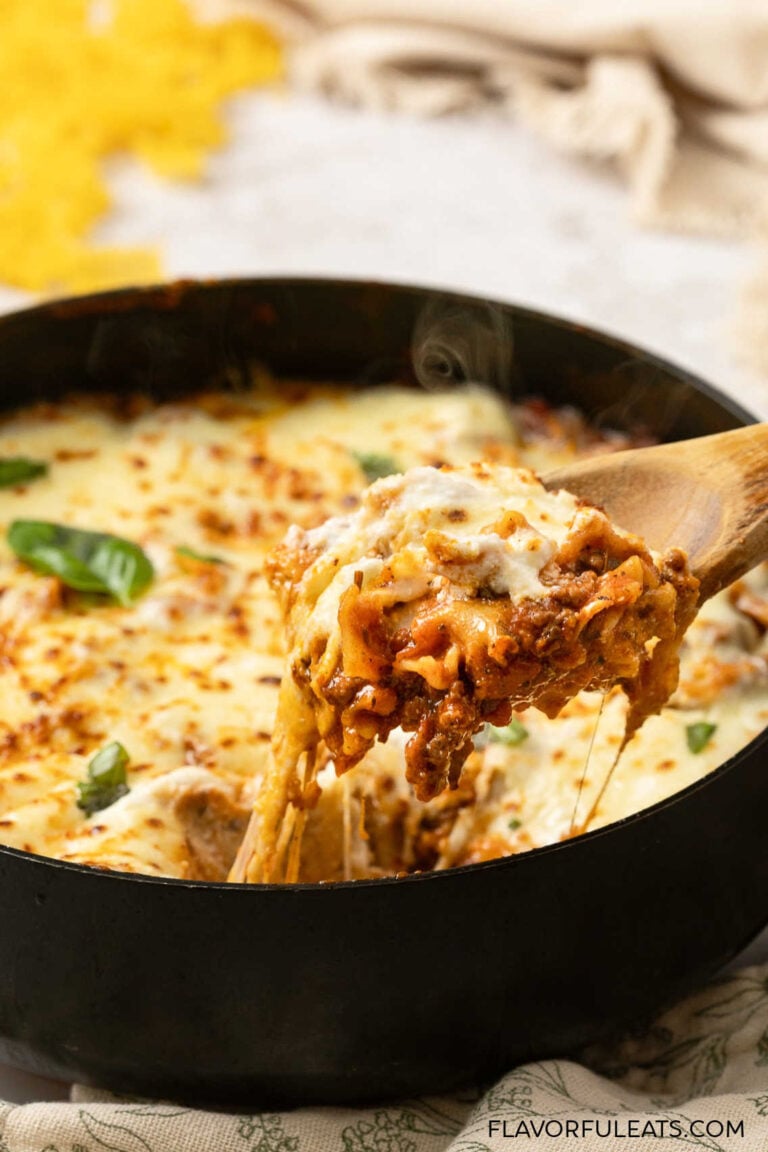 A serving spoon with a cheesy pull of One-Pan Cheesy Lasagna Skillet coming out of the pan.