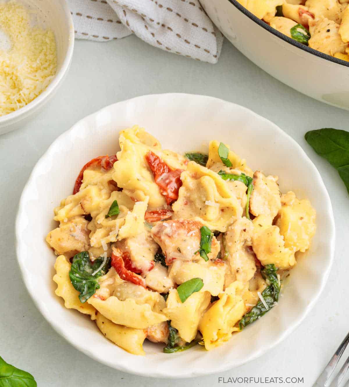 One-Pan Creamy Chicken & Tortellini in a bowl with the pan and Parmesan in the background.