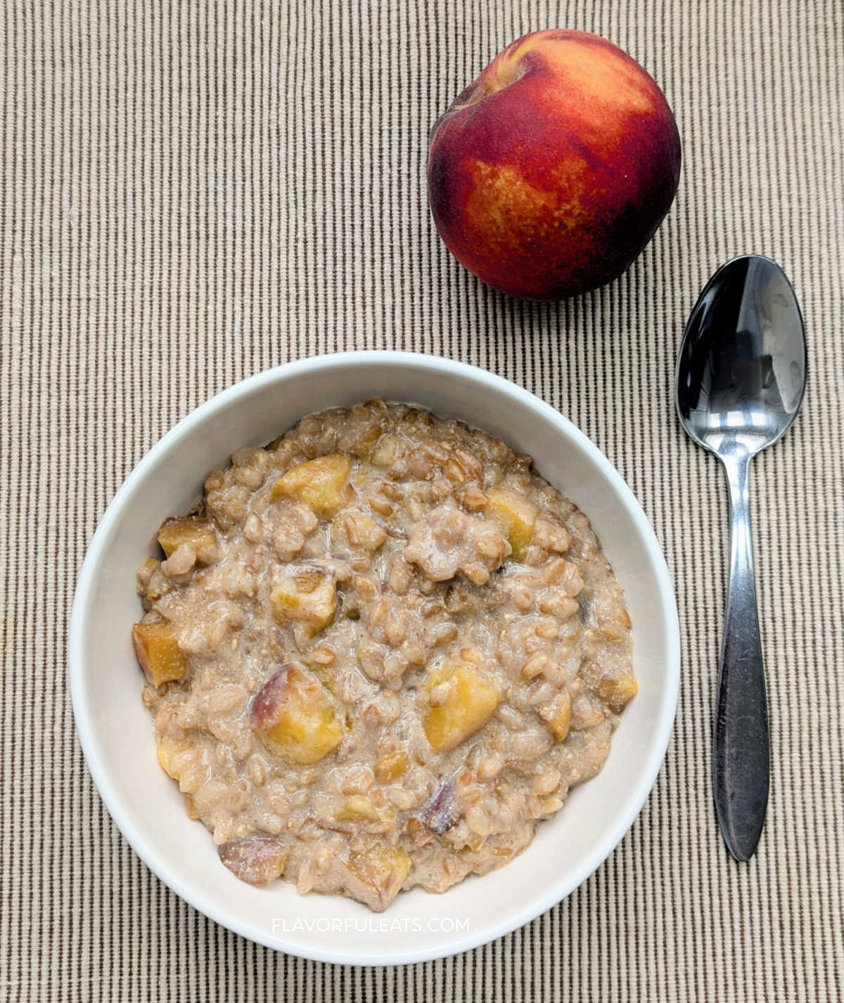 Slow Cooker Peaches & Cream Farro on a placemat with a peach and spoon beside it.