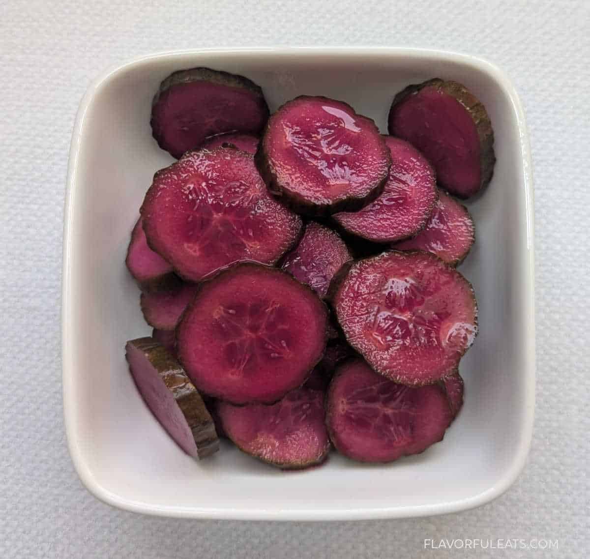 Pink Pickled Cucumbers up close in a small white bowl.