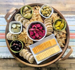 Pink Pickled Cucumbers on a serving board with cheese, crackers, and olives.