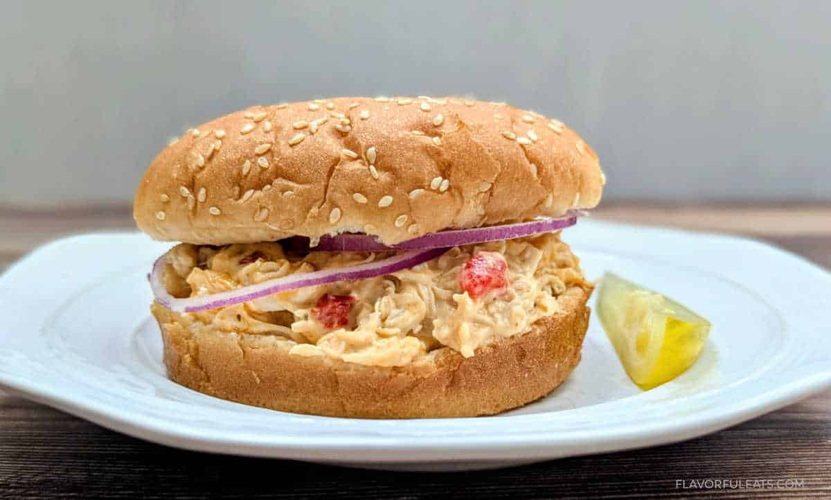 Slow Cooker Pimento Cheese Chicken Sandwich on a plate with a pickle.