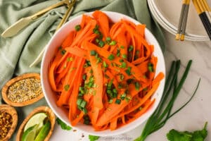 Ginger Sesame Carrot Ribbon Salad in a white bowl with fresh herbs on top.