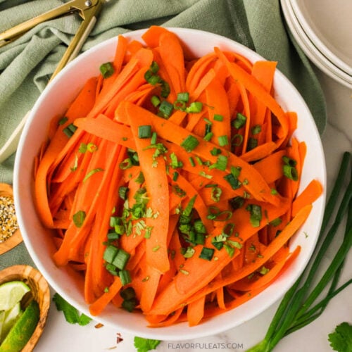 Ginger Sesame Carrot Ribbon Salad in a white bowl with fresh herbs on top.