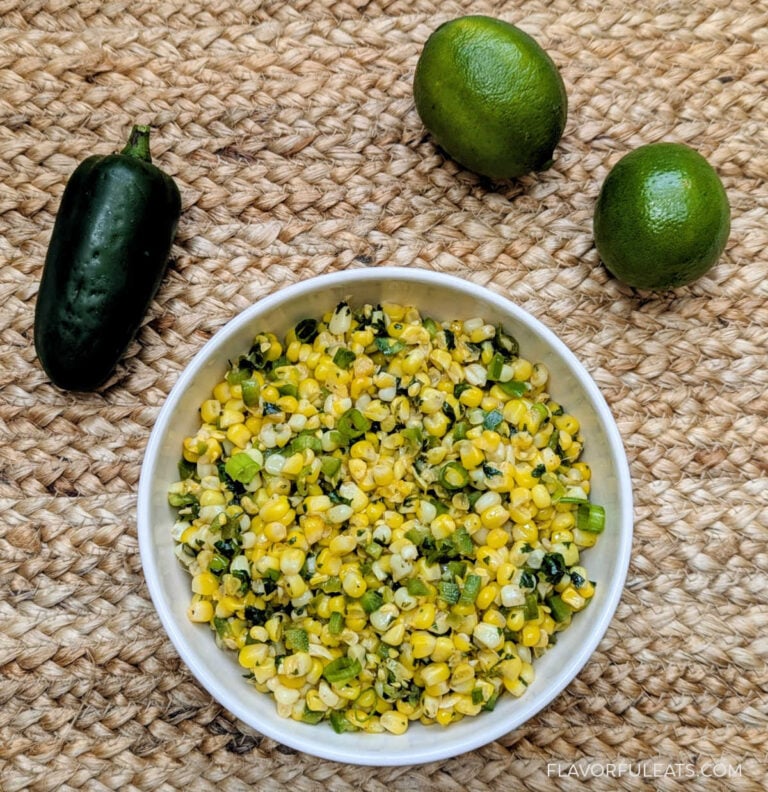 Slow Cooker Jalapeno Lime Corn in a white bowl on a placemat with limes and a jalapeno beside it.
