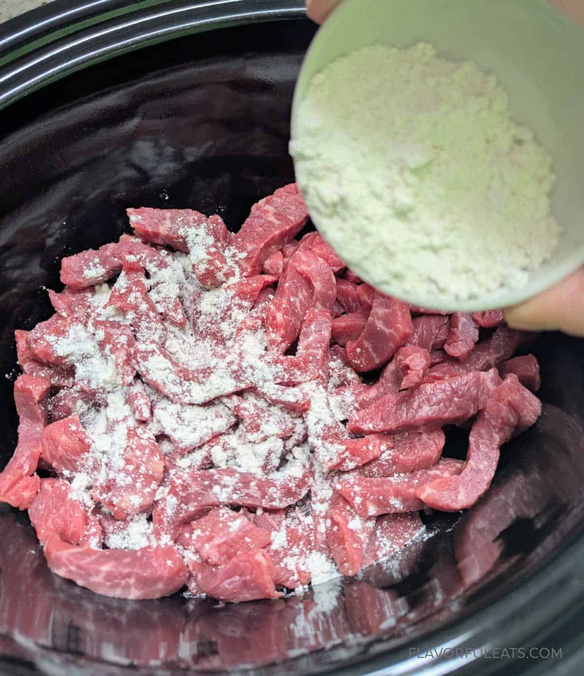 Flour being added to strips of beef in a slow cooker for Slow Cooker Lomo Saltado.