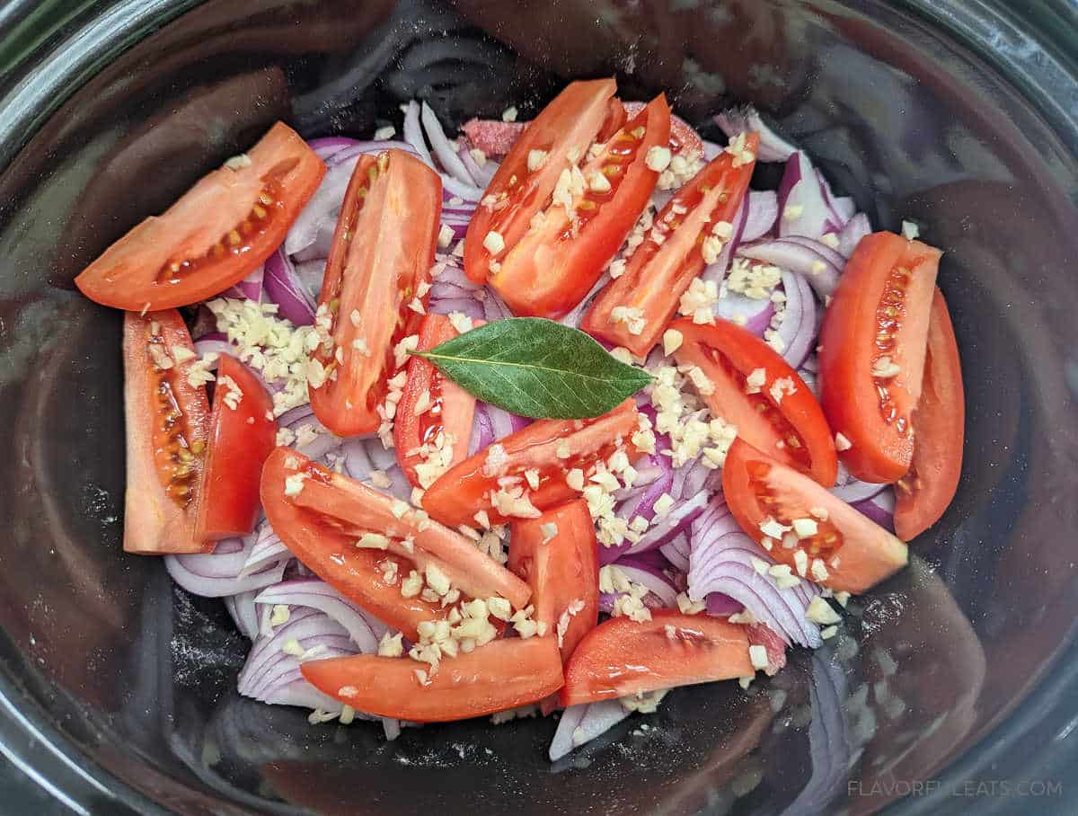 Onions, tomatoes, garlic, and bay leaves added to the floured beef strips in the slow cooker for Slow Cooker Lomo Saltado.