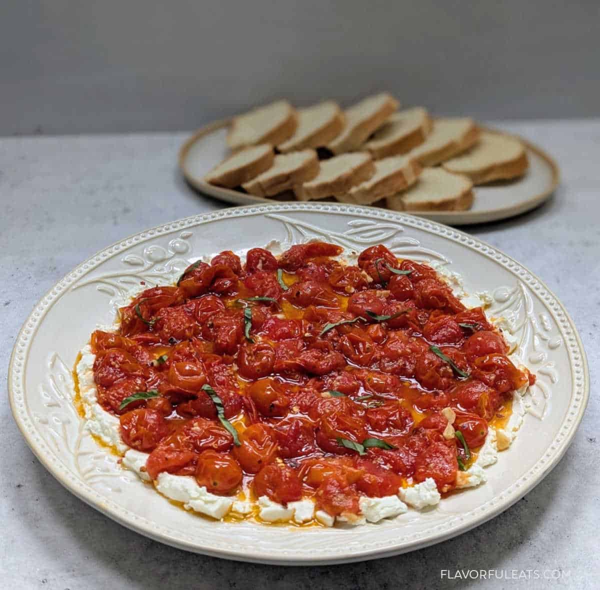 Roasted Cherry Tomato Goat Cheese Dip served on a platter with a tray of bread in the background.
