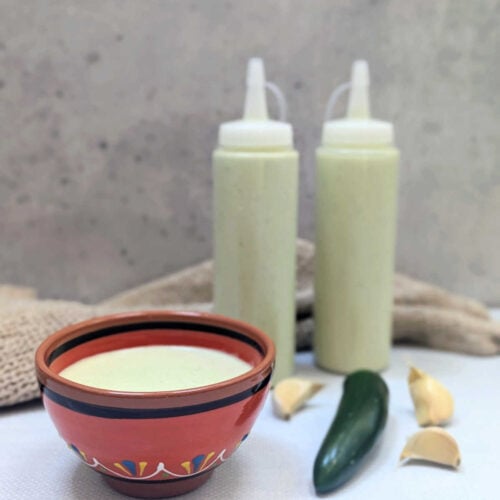 Creamy Serrano Garlic Sauce in a small bowl and in squeeze bottles.