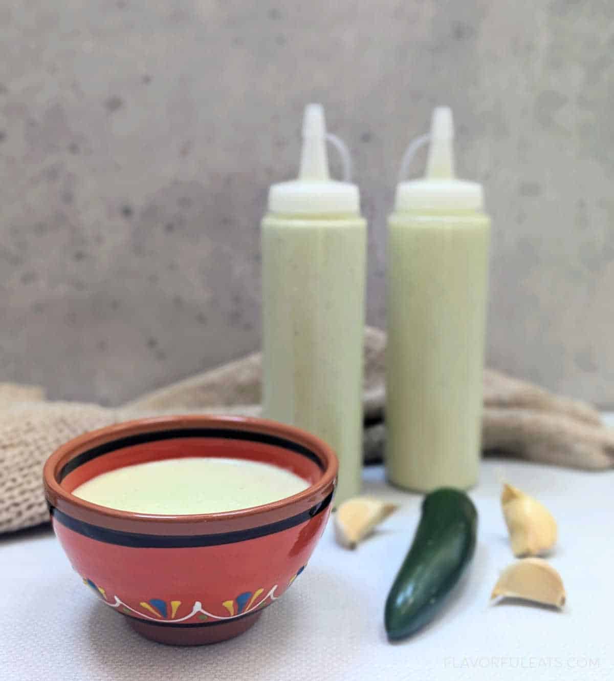 Creamy Serrano Garlic Sauce in a small bowl and in squeeze bottles.